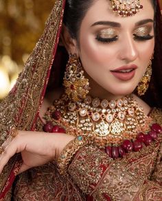 a woman in a red and gold bridal outfit with her hands on her shoulder