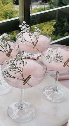 four wine glasses with flowers in them sitting on a table next to each other,