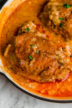 two meatballs covered in sauce and garnished with parsley