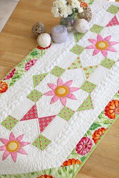 a quilted table runner with flowers on it and two small vases next to it