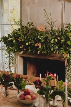 the table is set with fruit and greenery, candles are lit in front of the fireplace