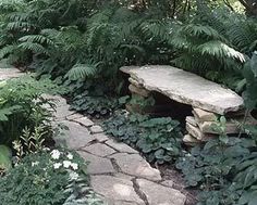 a stone path in the middle of a forest with a bench on one side and trees to the other