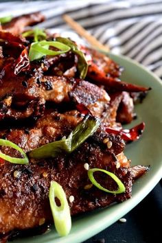 a plate filled with meat and vegetables on top of a striped table cloth next to chopsticks