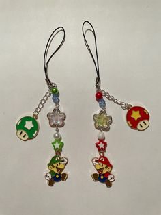 four charms are hanging from a chain on a white surface, one has a mario and the other is a mushroom