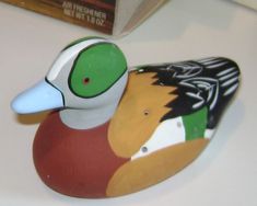 a wooden duck sitting on top of a white counter next to a book shelf and a bag