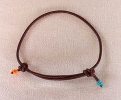 a brown leather bracelet with two blue and orange beads on it's end, sitting on a white surface