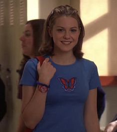 a woman with a butterfly on her shirt is standing in front of a mirror and smiling at the camera