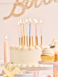 a table topped with lots of cupcakes covered in frosting and lit candles