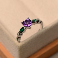 a purple ring with green and white stones sits in a box on top of a table