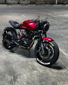 a red and black motorcycle parked on top of a cement parking lot next to a building