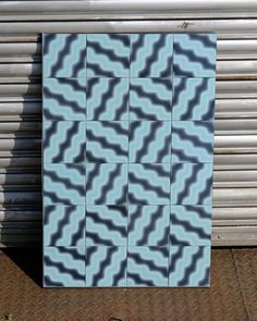 a blue and white square tile sitting on top of a brick sidewalk next to a building