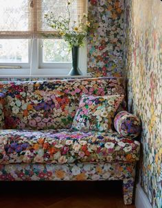 a floral couch sitting in front of a window next to a vase with flowers on it