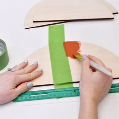 a woman is using a brush to paint the side of a piece of wood with green tape