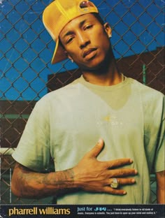 a man wearing a yellow hat and holding his hand on his chest in front of a chain link fence