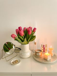 pink tulips in a white vase on a table with candles and other items