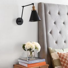 a bed with two books and a lamp on the headboard, next to a flower vase