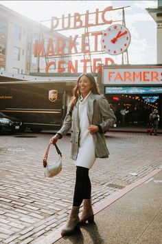 a woman is walking down the street in front of a market center with a clock