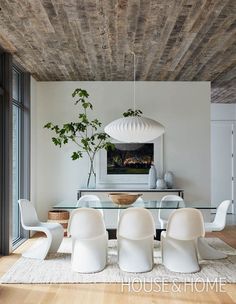 a modern dining room with white chairs and a glass top table surrounded by wood plank ceilinging