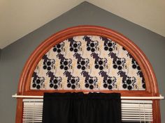 an arched window with black curtains in front of it and a floral pattern on the curtain valance