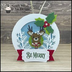 an ornament with a reindeer and holly on it, hanging from a wooden table