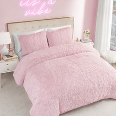 a bed with pink comforter and pillows next to a neon sign that says it's a nice day