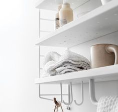 a shelf with towels, cups and mugs on it in a white bathroom area