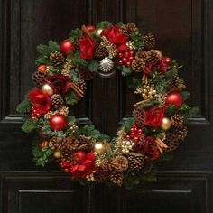 a christmas wreath is hanging on the front door with pine cones, berries and other decorations