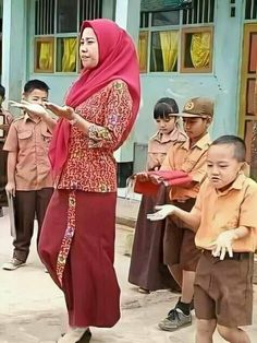 a woman in a red hijab standing next to other children wearing brown outfits