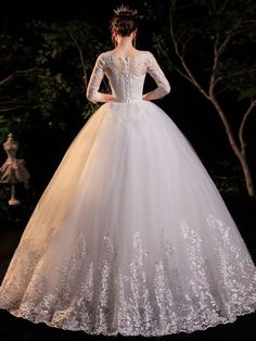 a woman in a white wedding dress standing on a dark surface with trees behind her