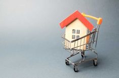 a miniature house in a shopping cart on a gray background with copy space for text