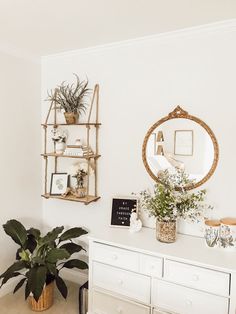 a white dresser and mirror in a room with plants on the top shelf next to it