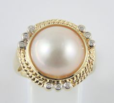 This is a 14 Kt yellow gold Mabe Pearl and Diamond ring. A Mabe Pear with a pink rose colorl is bezel set in the center. There is a double rope edging around the pearl with nine round full cut Diamonds bezel set in three groups. The ring has an open back and a tapered shank with a high polished finish.  The ring is size 7 The total weight is 6.13 grams. Marked : 585  14K Inventory # 1616 Mabe Pearl, Pearl And Diamond Ring, Beaded Jewelry Designs, Bezel Diamond, Multi Stone Ring, Natural Pearls, 14kt Gold, Jewelry Designs, Pink Rose