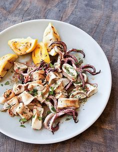 an octopus salad on a white plate with lemon wedges and parmesan cheese