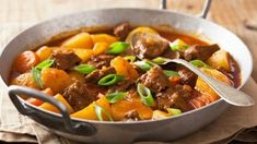 a bowl filled with meat and vegetables on top of a wooden table next to a spoon