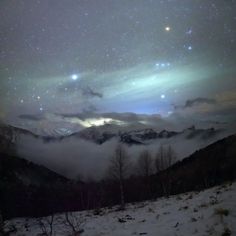 the night sky is filled with stars and clouds, as seen from a snowy mountaintop