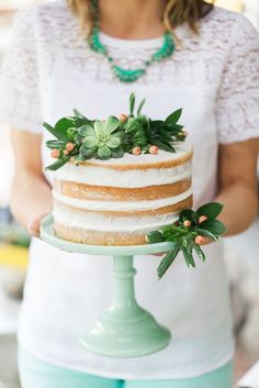 a woman holding a cake with succulents on it and greenery on top