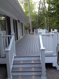 a white porch with steps leading up to the front door and back deck area that is surrounded by trees