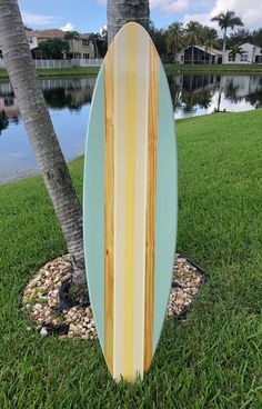 a surfboard is leaning against a tree in the grass near water and palm trees