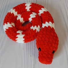 a red and white knitted snake toy sitting on top of a wooden table next to it's head