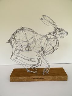 a wire sculpture of a dog on a wooden base