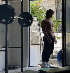 a shirtless man standing in front of a gym machine and looking out the window