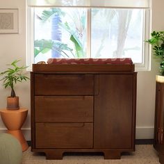 a baby crib in front of a window with potted plants on the side