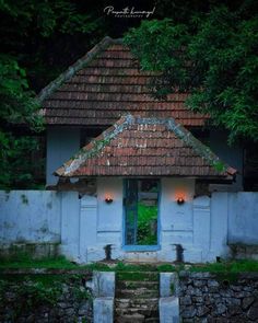 an old building with a green door and window in the middle of it, surrounded by trees