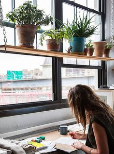 a woman sitting at a desk in front of a window with plants on the ledge