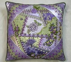 a decorative purple and green pillow on a white surface with flowers in the center,