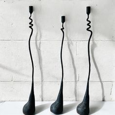 three black vases sitting next to each other on a white counter top in front of a brick wall