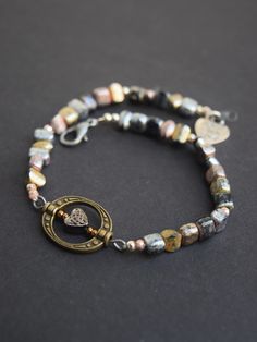 Made with metallic beads repurposed from a necklace found at an antique shop. This bracelet features a small Celtic heart bead at the center. This would make a perfect gift for a loved one and is subtle enough to be worn everyday.  Specific coloring and bead shapes will vary. Make it a matching set with our Black Lariat Necklace: https://www.etsy.com/listing/960812469/black-lariat-necklace?ref=shop_home_active_1&frs=1 Your bracelet will be packaged in a cotton stuffed cardboard box. Is this a gift? We would love to wrap your gift for you! Select the occasion under the Gift Wrapping option. Metal Beaded Bracelets With Heart Beads, Vintage Bracelets With Heart Beads For Gift, Vintage Nickel-free Beaded Bracelets With Round Beads, Vintage Nickel-free Beaded Bracelets, Beaded Heart Bracelet, Dark Bracelet, Bead Shapes, Inspirational Rocks, Dark Jewelry