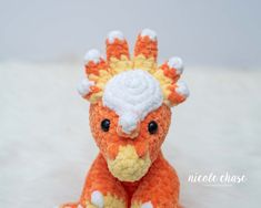 an orange and white crocheted dragon sitting on top of a white blanket with its eyes closed