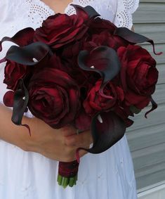 a woman holding a bouquet of red roses and calla lilies in her hands