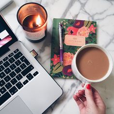 a woman holding a cup of coffee next to a laptop computer and candle on a marble table